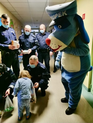 Zdjęcie przedstawia umundurowanych policjantów i Sznupka wręczających dziecku cukierki.