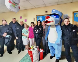 Zdjęcie przedstawia Sznupka oraz umundurowanych policjantów z przekazanymi prezentami dla dzieci.